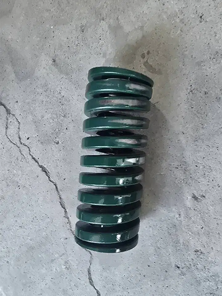 JIS green die spring with 2.7% permanent set (free height reduced from 150mm to 146mm) caused by exceeding 24% compression limit. Spring operated at 38mm stroke in stamping die, 2mm beyond safe 36mm maximum, resulting in catastrophic failure at 20,000 cycles. Visual evidence of fatigue damage and plastic deformation from overstress.